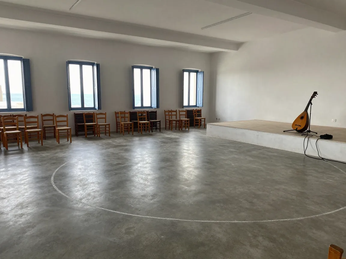 Empty Greek reception hall with polished floor, chairs along walls and a small stage holding a bouzouki.